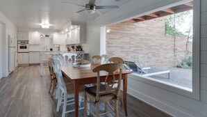 A modern kitchen with white cabinets, a wooden dining table, and a view of a brick wall and outdoor area. - Private Beach • Hot Tub • Sauna • Game Room •  No-Wake Cove + Party Cove Access (Coloma)