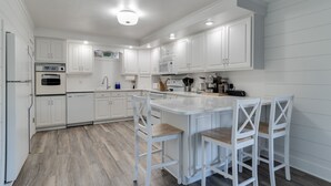 A modern kitchen with white cabinetry, a central island with bar stools, and built-in appliances. - Private Beach • Hot Tub • Sauna • Game Room •  No-Wake Cove + Party Cove Access (Coloma)