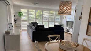 Een moderne woonkamer met een donkergrijze bank, een ronde glazen tafel met stoelen, en een rieten mandje op de tafel.