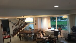Een moderne woonkamer met een eethoek, een trap en een groot raam met uitzicht op een tuin.