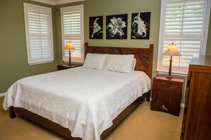 Un letto rifatto con cura, con una coperta bianca, affiancato da due comodini con lampade, in una stanza dalle pareti verdi e tre quadri floreali incorniciati sopra il letto.