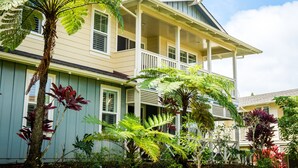 A two-story house with a porch, surrounded by lush greenery. - Spacious condo with Central AC, beautiful pool and relaxing hot tub (Princeville)