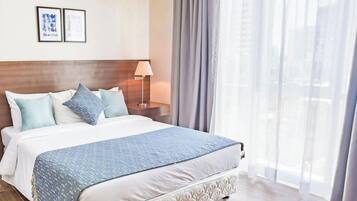 A hotel room with a large bed, a nightstand, a lamp, and a window with curtains.