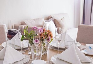 Mesa de comedor decorada con servilletas blancas, platos y copas, un jarrón con flores, y un correo electrónico y sitio web de Apexotelrooms.