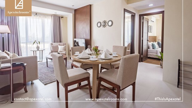 A modern master bedroom with a dining area, a TV, and a large window with curtains.