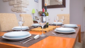 Een eettafel gedekt met borden, glazen en bestek, met een fles wijn en een houten dienblad in het midden.