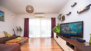 Een woonkamer met een bank, salontafel, televisie en decoratieve planten.