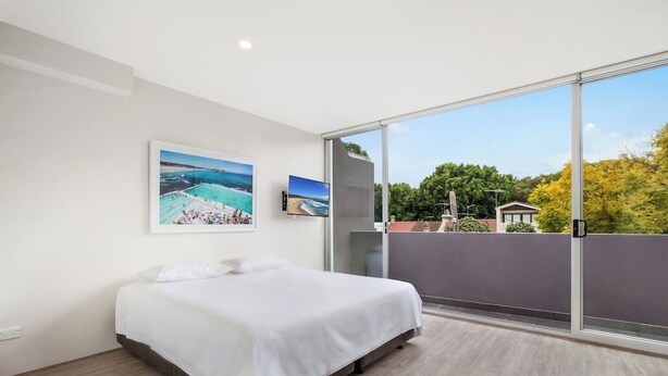 A bedroom with a bed, a large window, and two framed pictures on the wall.