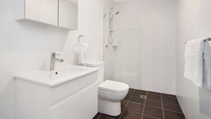 A modern bathroom with a white sink, toilet, and shower area.