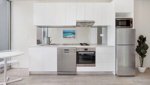 A modern kitchen with white cabinetry, stainless steel appliances, and a small dining area with a white table and chairs.