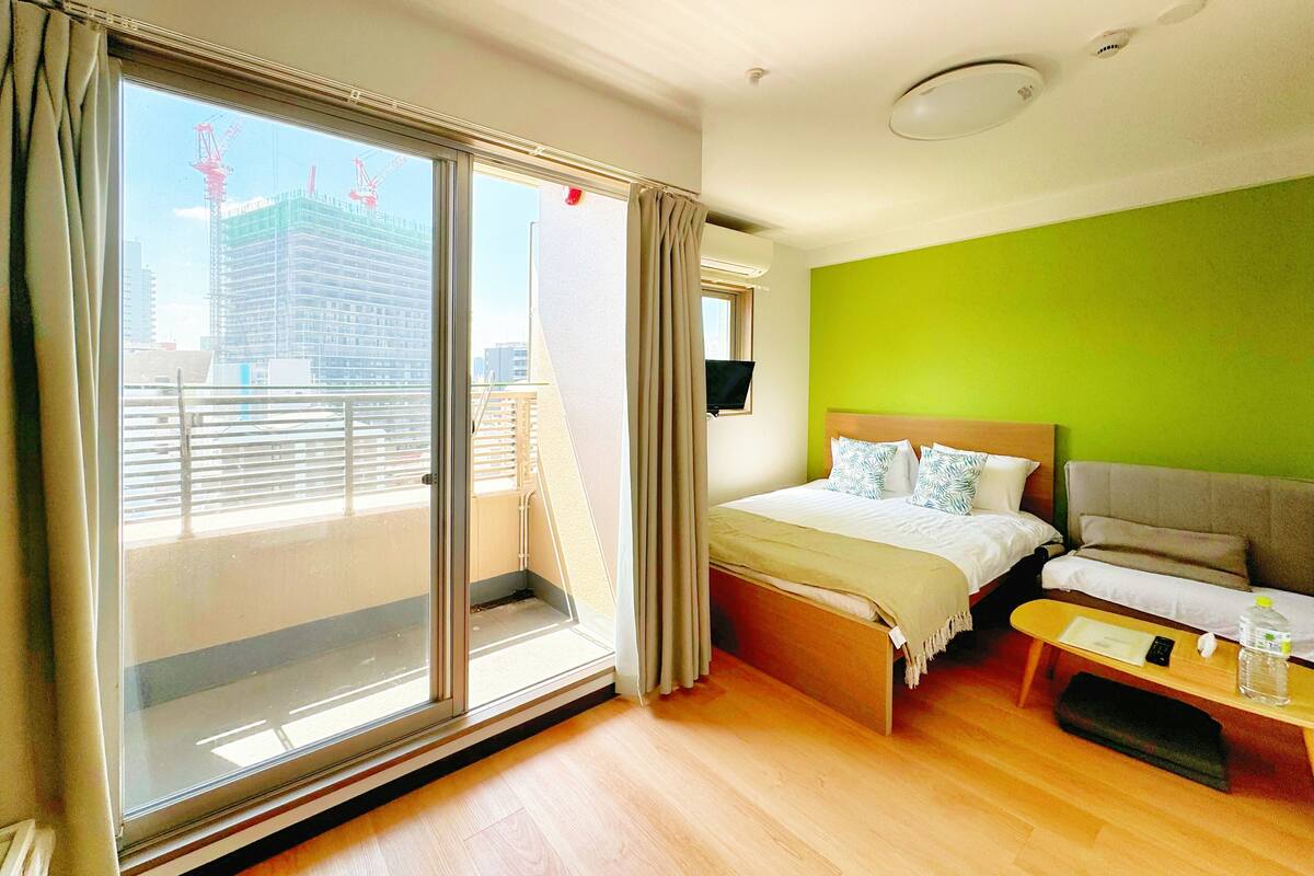 A hotel room with a bed, a sofa, a small table, and a balcony with a view of a construction site.