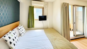 Une chambre d’hôtel équipée d’un lit, d’un téléviseur à écran plat fixé au mur, d’une fenêtre avec des rideaux et d’une porte-fenêtre coulissante.
