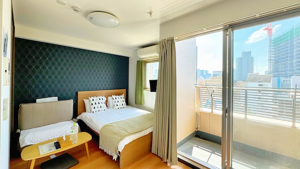 Une chambre d’hôtel avec un lit, une petite table et une chaise, une fenêtre donnant sur la ville et un balcon avec une balustrade.