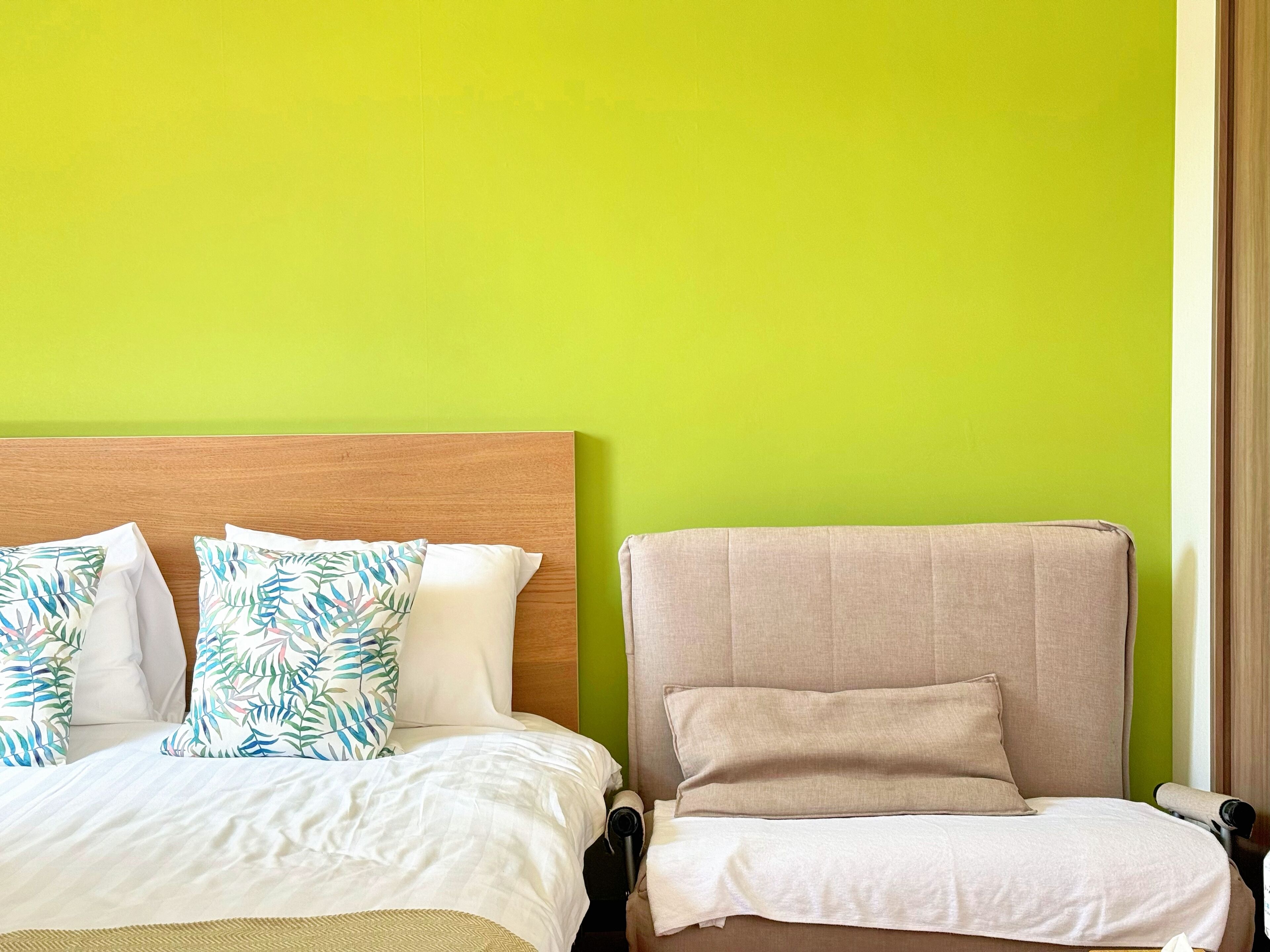 A hotel room with a bed, a chair, and a bright green wall.