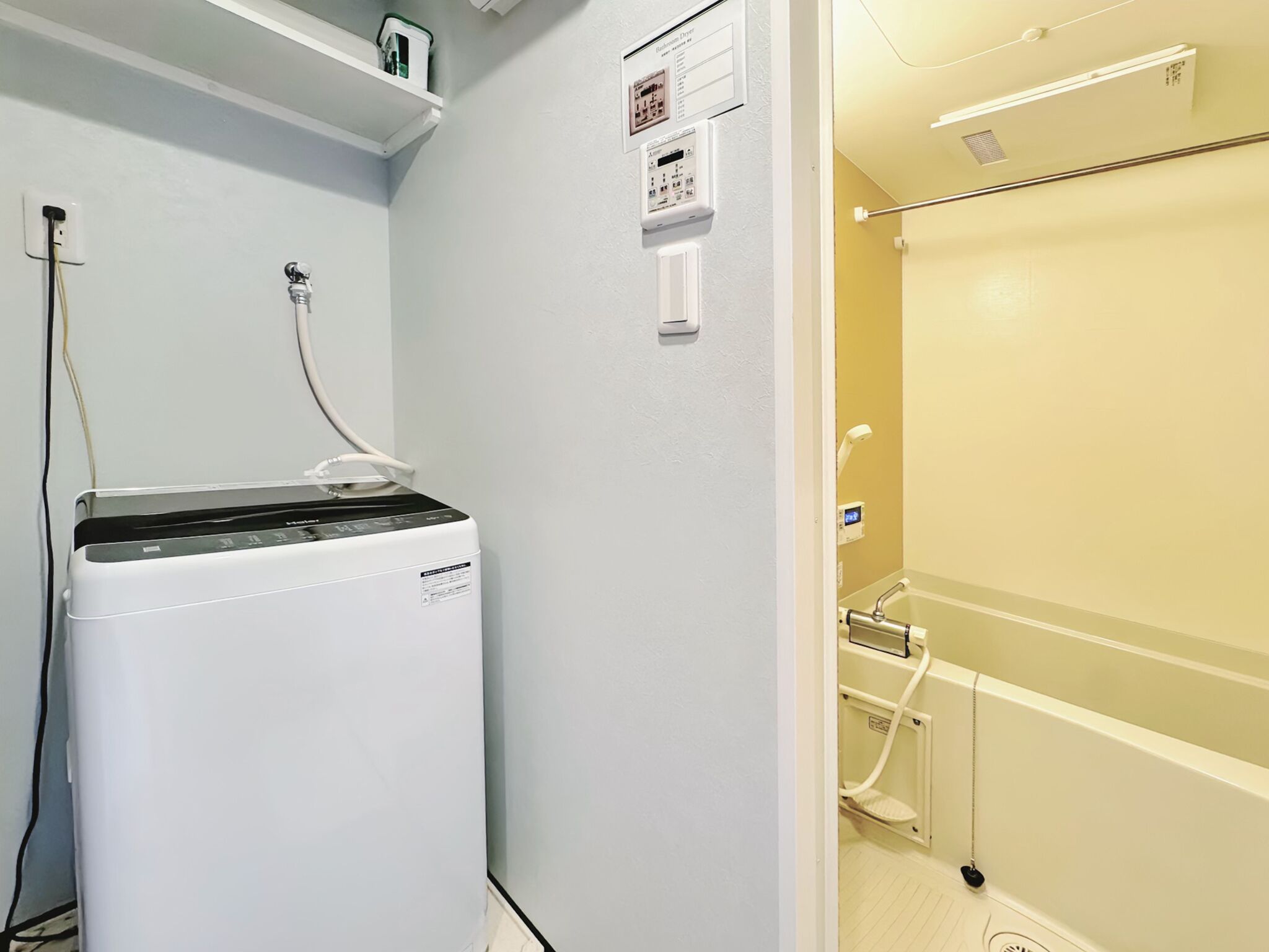 A laundry room with a front-loading washer and dryer, a shelf with toiletries, and a control panel on the wall.