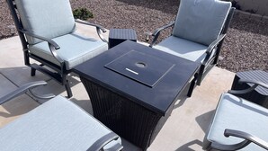 Un patio con dos sillas acolchadas de azul claro, una mesa negra y una cesta de mimbre negra.