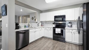 Una cocina moderna con armarios blancos, un refrigerador negro, un microondas y un lavavajillas.