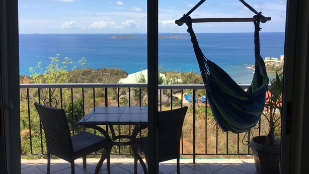 A balcony with a view of the ocean, a hanging chair, and a table. - Sunrises & Sunsets Tropical Getaway - Incredible Views Overlooking Caribbean Sea (St. Thomas)