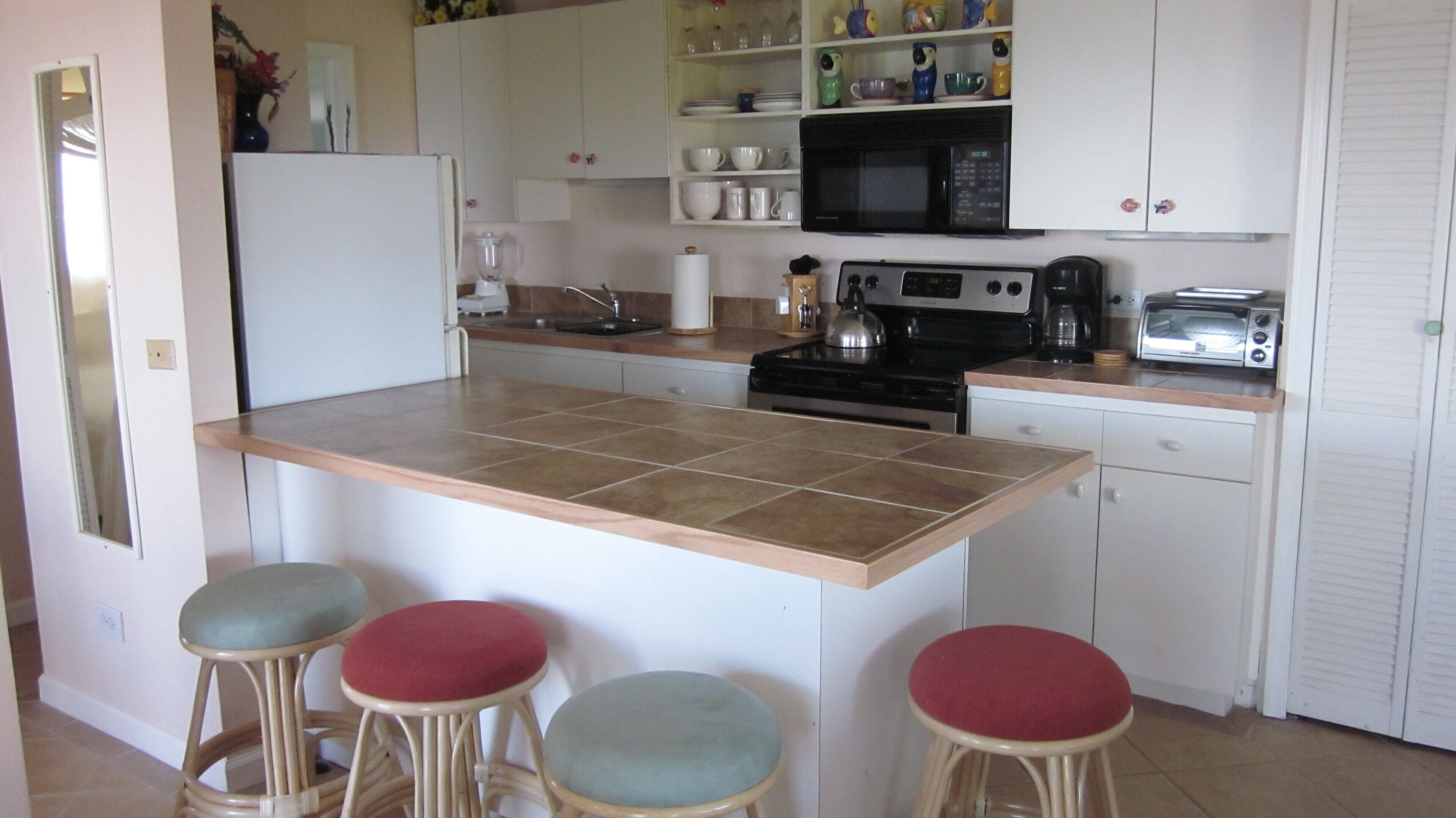 Cocina compacta con una isla central, refrigerador, microondas, estufa y taburetes de bar.