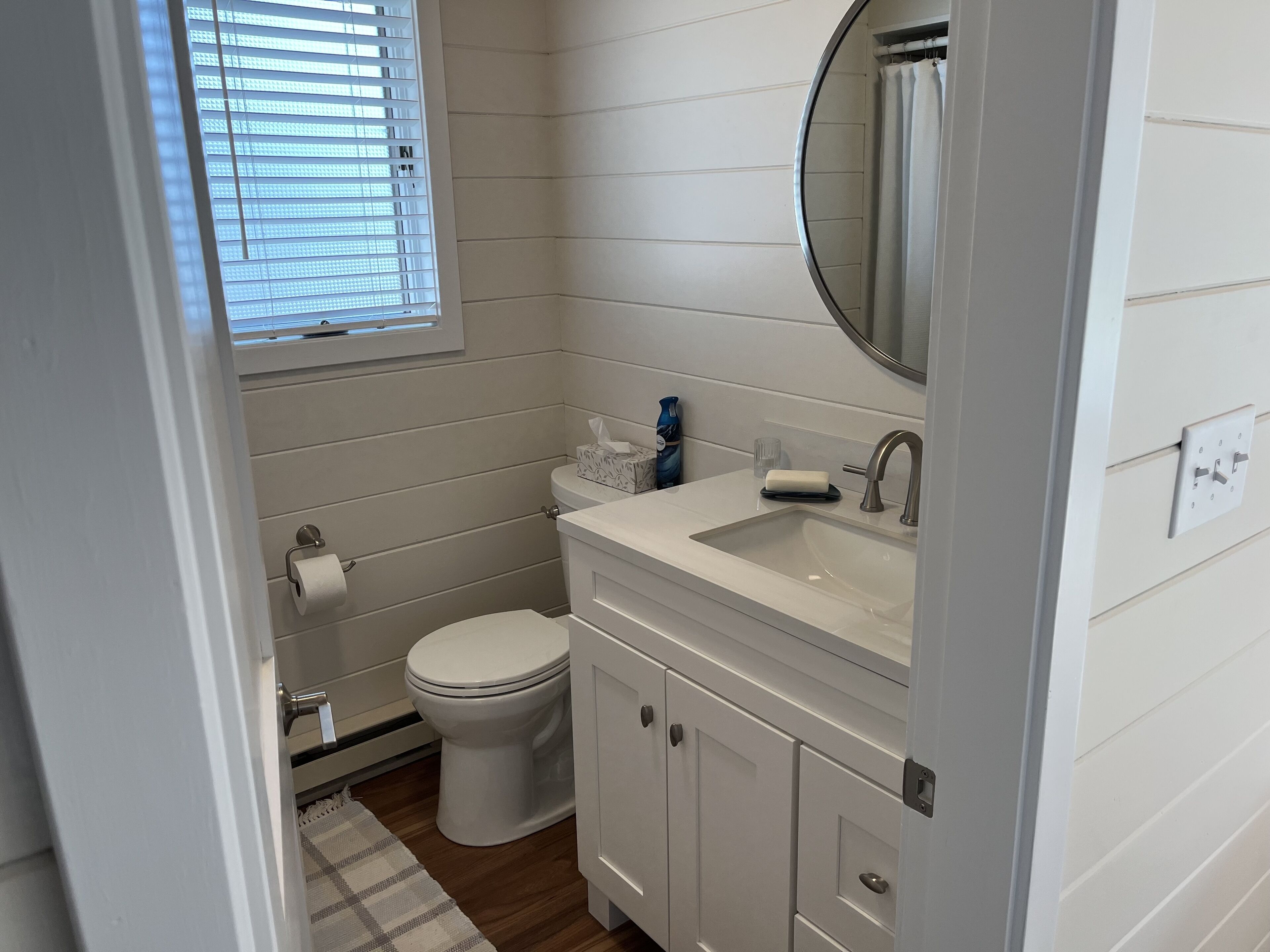 A bathroom with a toilet, sink, mirror, and window with blinds.