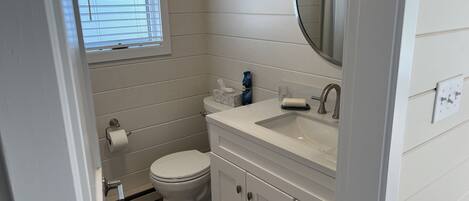 A bathroom with a toilet, sink, mirror, and window with blinds.