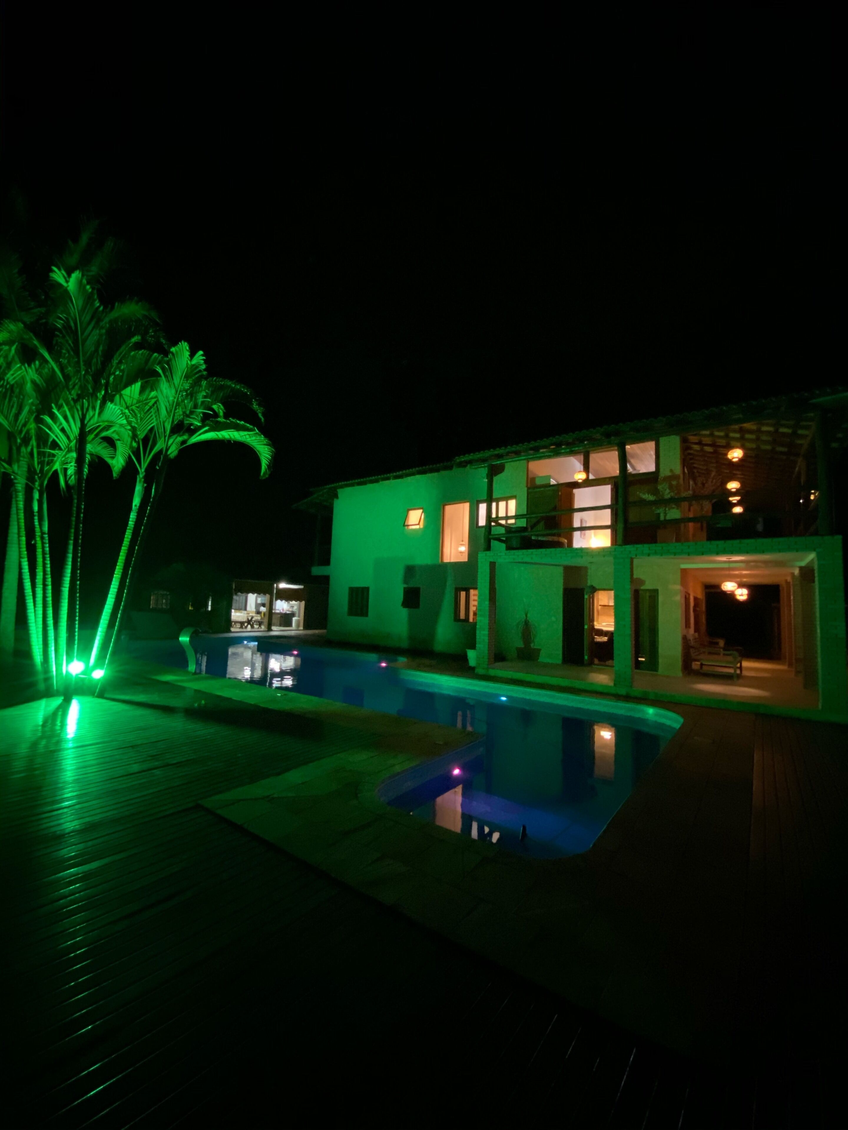 A modern house with a swimming pool, green lighting, and a well-maintained garden.