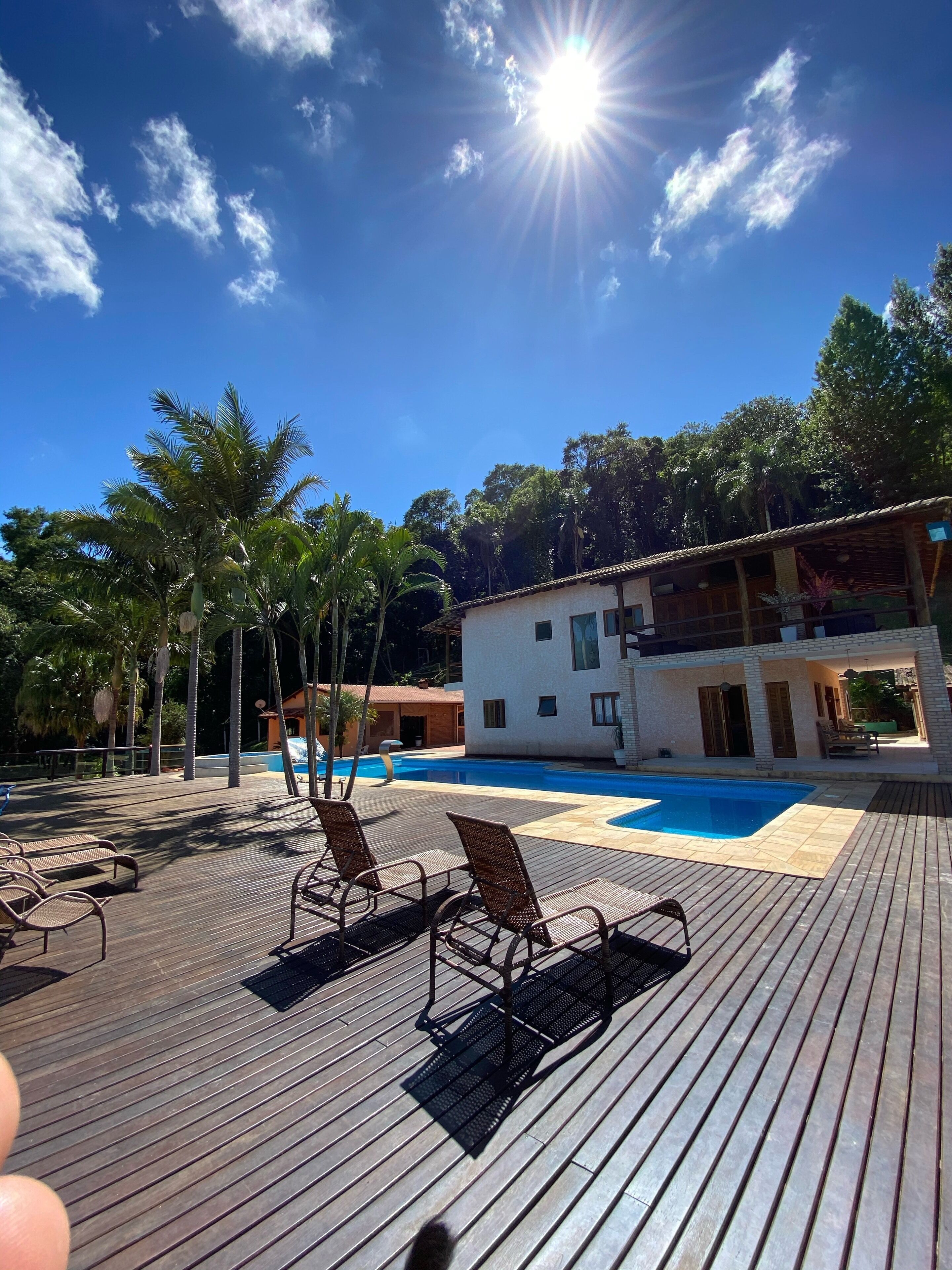 Una terraza de madera con sillones, una piscina y un edificio con balcón.