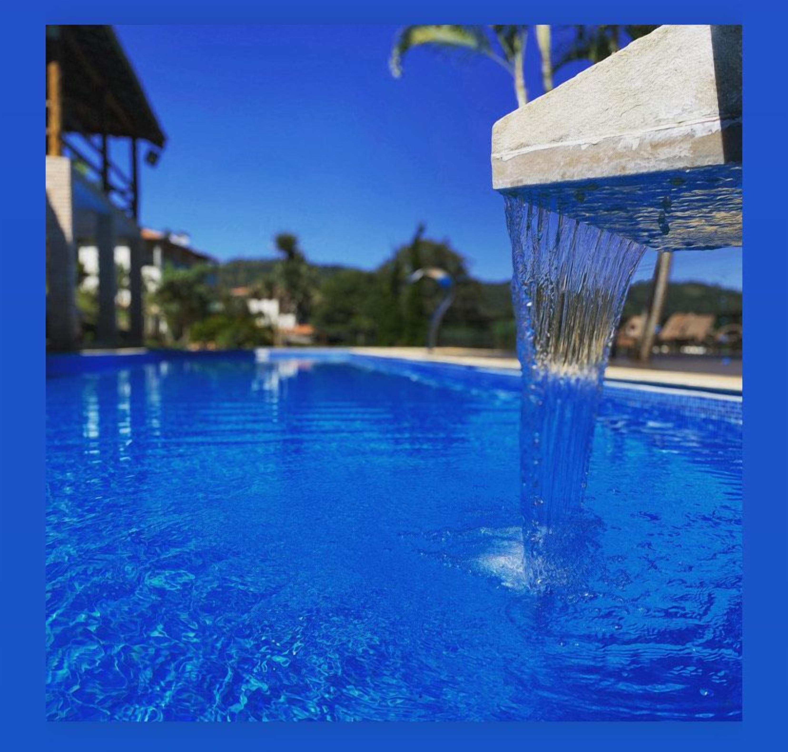 Ein klares, blaues Schwimmbecken mit Wasserspiel, umgeben von blauem Himmel und Palmen.