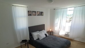 Un dormitorio con cama, mesita de noche, lámpara y vistas al exterior.