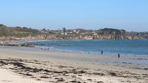A beach with a clear view of the sea and a distant town. -  Les Gîtes de Fabie : La Maison des gardiens de l'océan avec spa, face à l'océan (Plougonvelin)