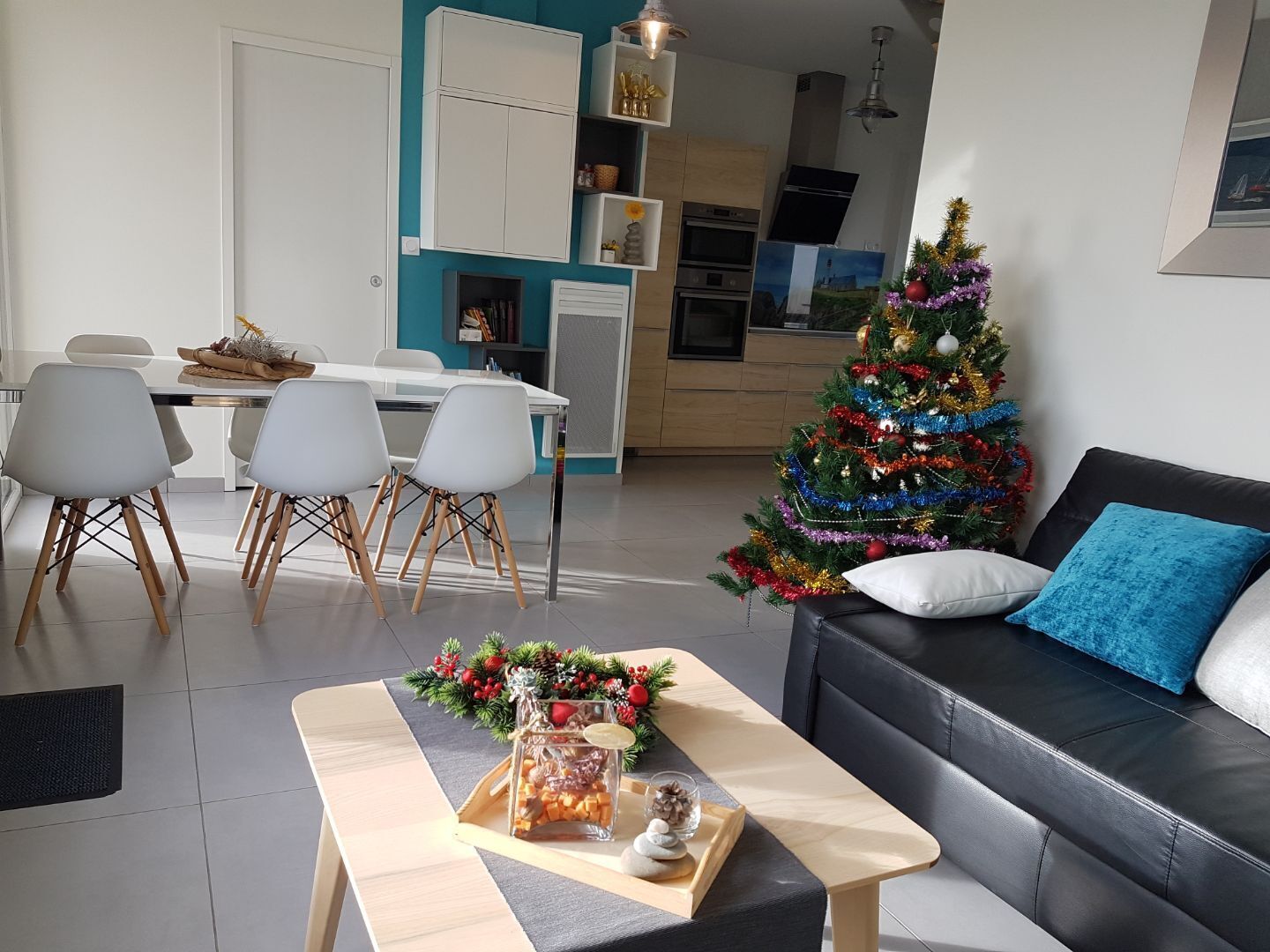 A modern living room with a black leather sofa, a wooden coffee table with a decorative centerpiece, and a Christmas tree.