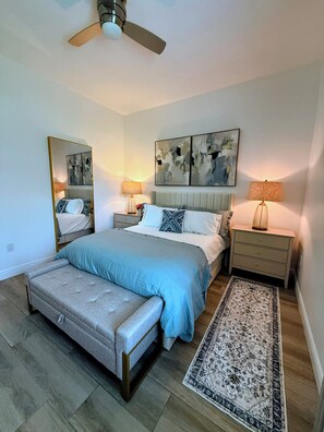 A bedroom with a bed, bedside tables, a ceiling fan, a bench, and a rug. - Lakefront Oasis. Sandy Beach and dock await your relaxation! (Odessa)