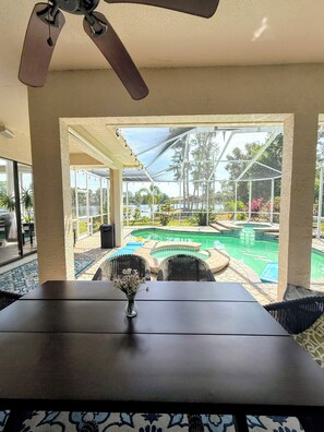 A covered patio with a table, chairs, and a view of a swimming pool and garden. - Lakefront Oasis. Sandy Beach and dock await your relaxation! (Odessa)