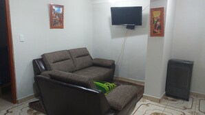 A living room with a brown sofa, a flat-screen TV mounted on the wall, and a small heater on the floor. - Filfor Hause (Cusco)