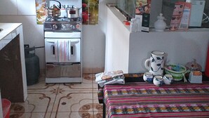 A small kitchen with a stove, a refrigerator, and a window. There is a table with a colorful tablecloth and a few items on it. - Filfor Hause (Cusco)