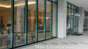Vue de l’entrée principale d’un bâtiment doté de grandes portes vitrées et d’un sol carrelé.