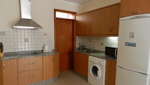 Una cocina con armarios de madera, una campana extractora de acero inoxidable, un microondas integrado, una lavadora y un refrigerador.