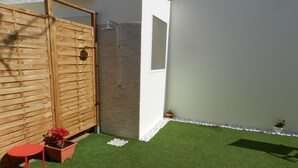 Un espacio exterior pequeño con césped artificial, un panel de madera, un taburete rojo y una planta en maceta.