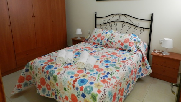 Un dormitorio con una cama, un armario de madera, dos mesitas de noche con lámparas y un cuadro en la pared.