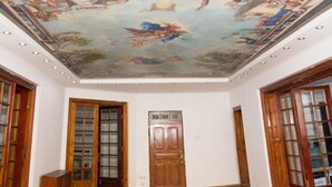 Una habitación amplia con suelo de parquet de madera, una puerta grande de madera y un mural en el techo.