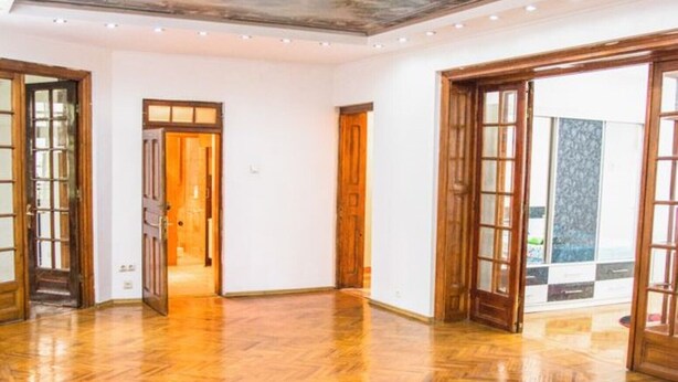Amplia habitación con piso de madera pulida, grandes puertas de madera y un techo alto con un mural detallado.