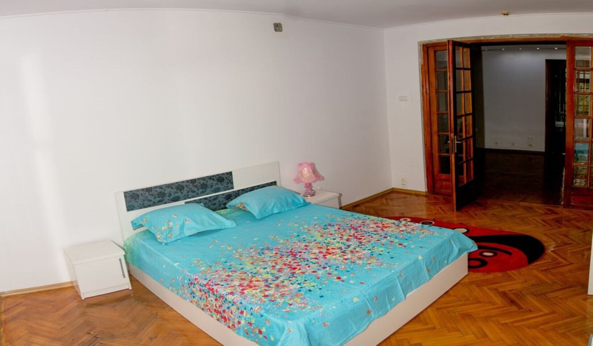 A bedroom with a bed, a nightstand, and a wooden floor.