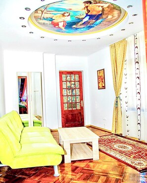 A room with a wooden floor, a green sofa, a small table, a red door with a decorative panel, and a ceiling mural. - Apartments Faryna is situated in the real heart of Bucharest  (Sector 1)