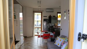 A modern kitchen with a dining area, a sofa with colorful cushions, and a view of a balcony.