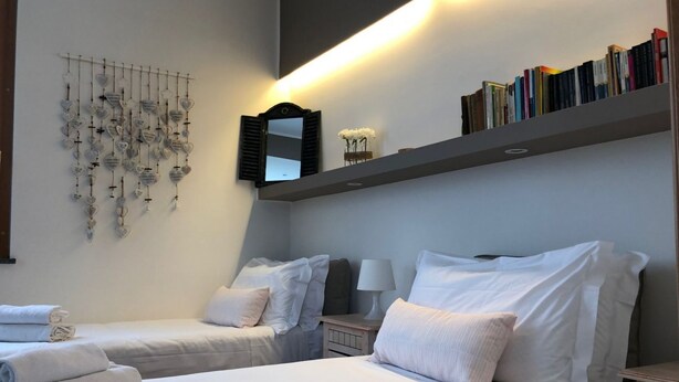 A hotel room with two beds, a wall-mounted mirror, a shelf with books, and a decorative wall hanging.