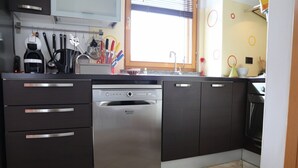 A modern kitchen with stainless steel appliances, dark cabinetry, and a window with blinds.