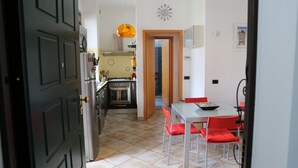 A modern kitchen with a dining area, featuring a table and chairs, a clock on the wall, and a door leading to another room.