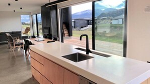 A modern kitchen with a large window, wooden cabinets, and a built-in dishwasher. - The Gem in Peninsula Bay (Wanaka)