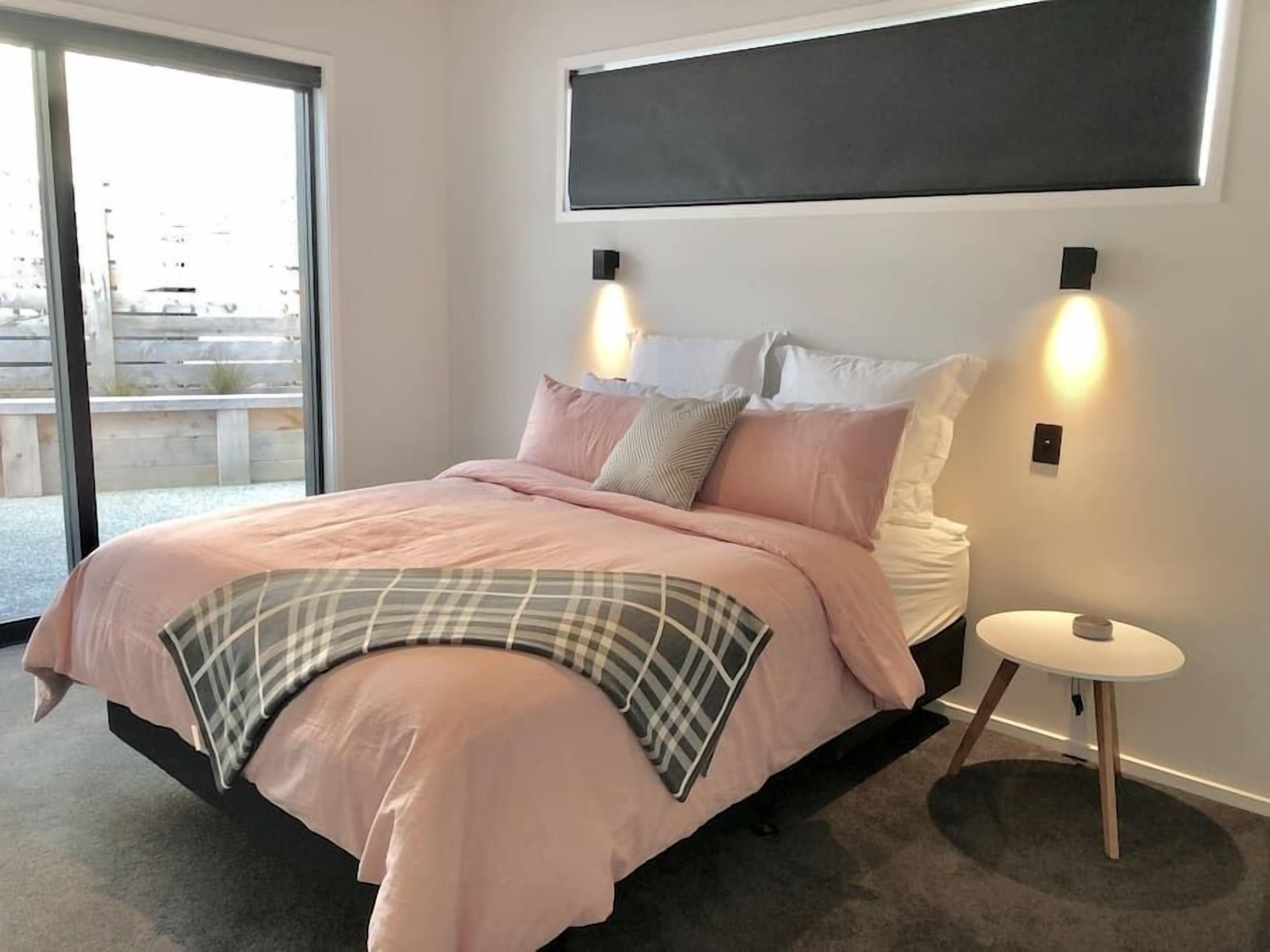 Een moderne slaapkamer met een groot bed, twee bedlampen en uitzicht op de omgeving via een schuifdeur.