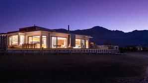 A modern house with large windows, a deck, and a mountain backdrop. - The Gem in Peninsula Bay (Wanaka)